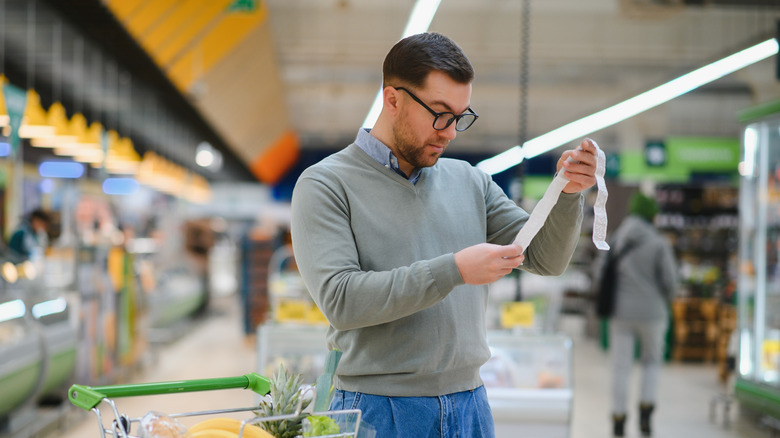 Surprised man reads a receipt in grocery store