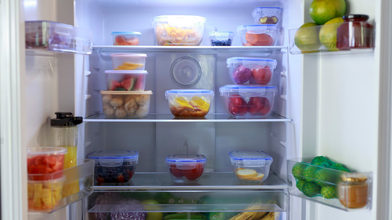 a fridge organized with tupperware and produce on shelves and in doors