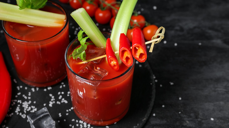Glasses of bloody mary cocktail with celery and chili pepper on black background