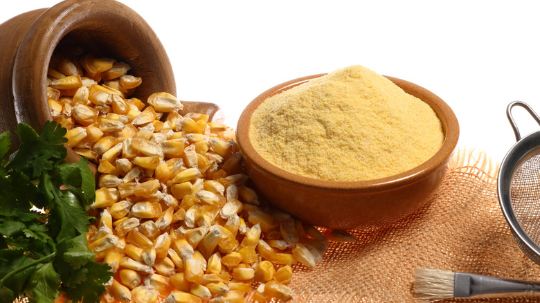 Corn kernels spilling out of a vessel next to a bowl of corn flour