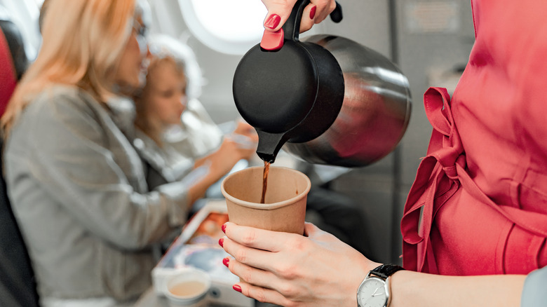 Flight attendant serving coffee in paper cup on airplane.