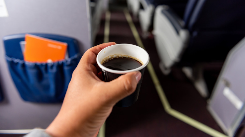 Cup of coffee on airplane held out in middle of aisle.