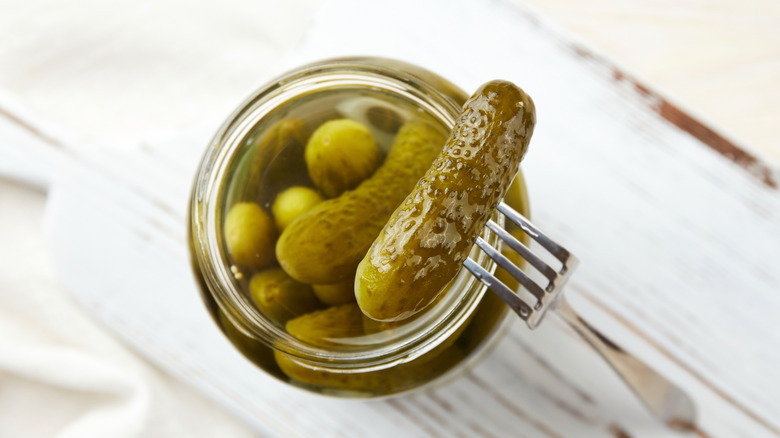 An illustrative image showing fermented pickles in a jar on a wooden background.