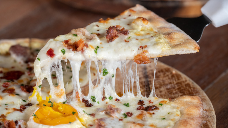 A slice of breakfast pizza pulled from the whole pie.