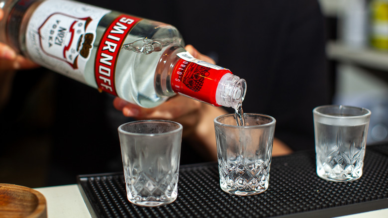 Person pouring shots of vodka on bar mat
