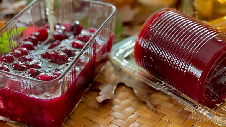 A glass dish filled with homemade cranberry sauce sitting next to a dish holding canned cranberry sauce that hasn't been sliced yet