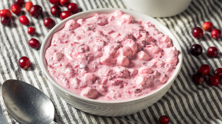 Cranberry fluff in a white bowl on a black and white striped towel with cranberries scattered around the bowl