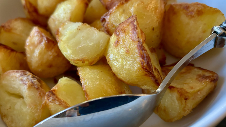 Chunks of roast potatoes in a bowl with a serving spoon