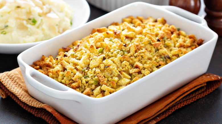 Stuffing in a white baking pan next to another pan filled with mashed potatoes on a dinner table