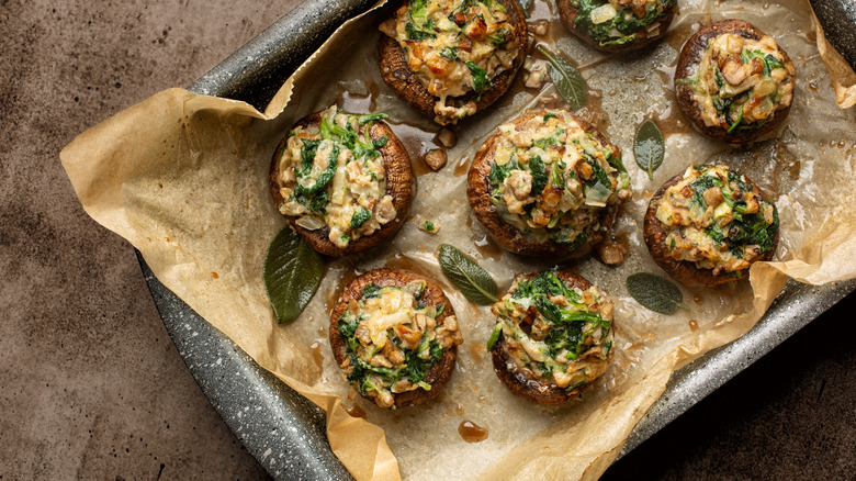 A pan of stuffed mushrooms on parchment paper are photographed from overhead.