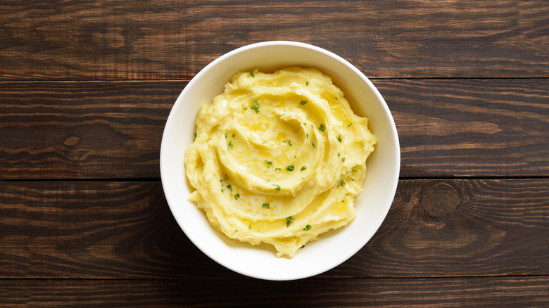 Garlic butter with herbs in white bowl on wood table.