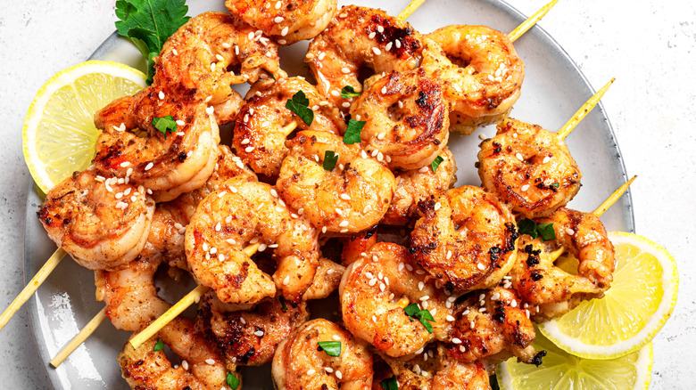 Grilled skewered shrimp on a plate with lemon slices