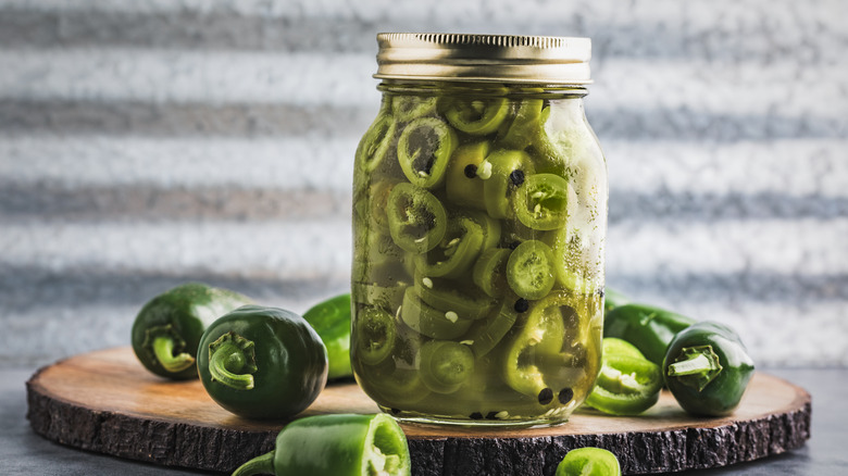 Jar of pickled jalapeños on a log slice next to fresh jalapeños