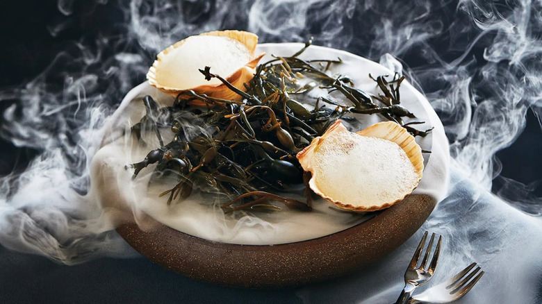 Scallops on a bed of seaweed surrounded by dry ice smoke
