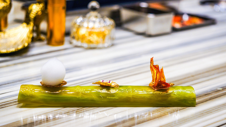 Three small desserts plated on a green stem of bamboo