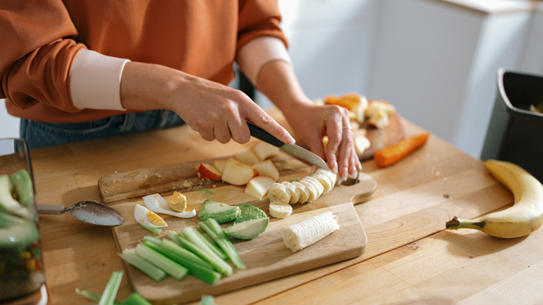 a woman slicing fruits and veggies on wooden cutting board