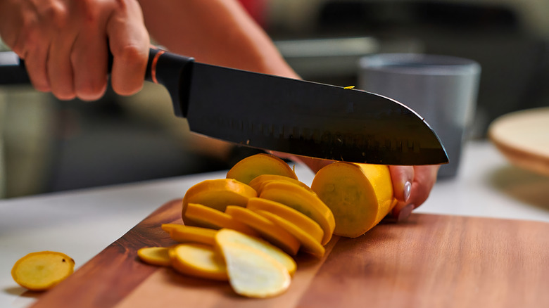 slicing a squash with a knife on wooden cutting board