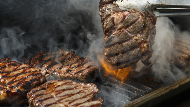 Steaks on a grill with someone flipping one over with tongs.