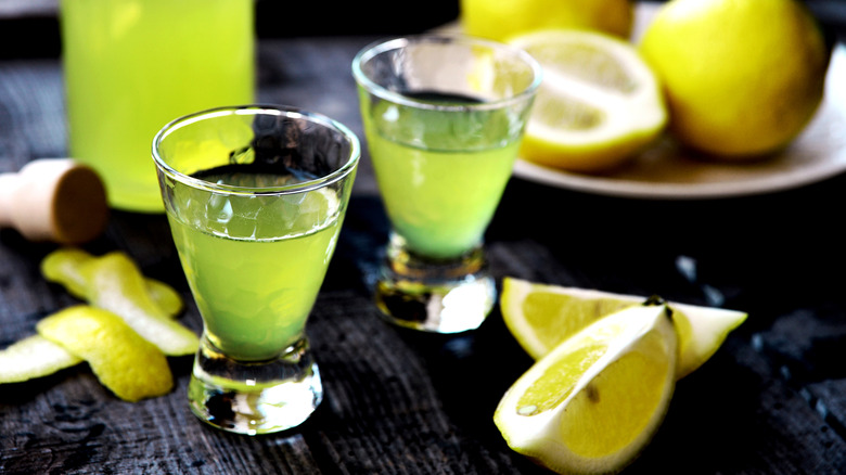 Two glasses of limoncello, with fresh lemon segments on a table
