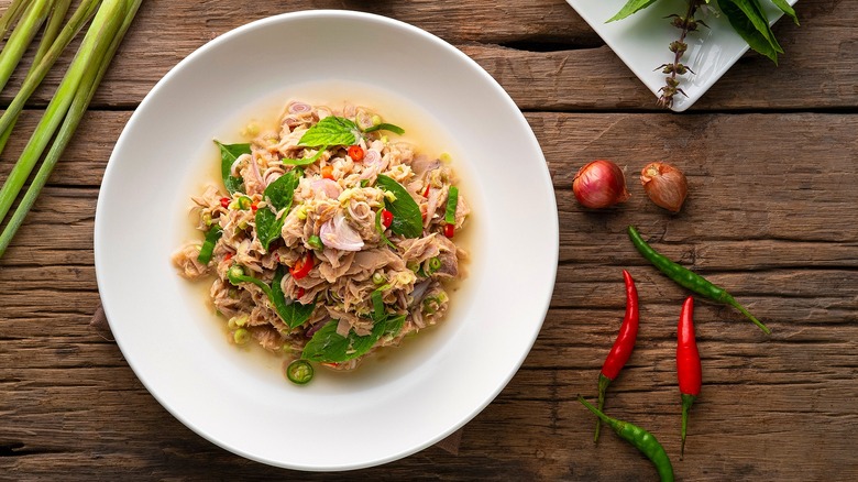 Top-down view of tuna salad mixed with Thai basil, lemongrass, chilies, and jalapeños in a shallow white bowl