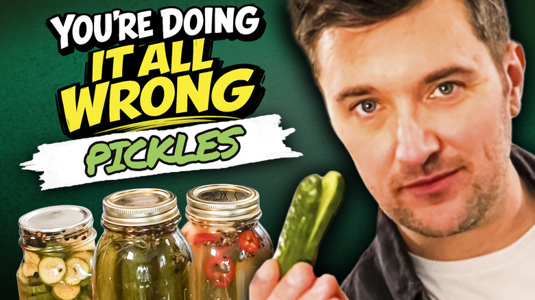 Man hold up pickles in front of mason jars of homemade pickles with spice.