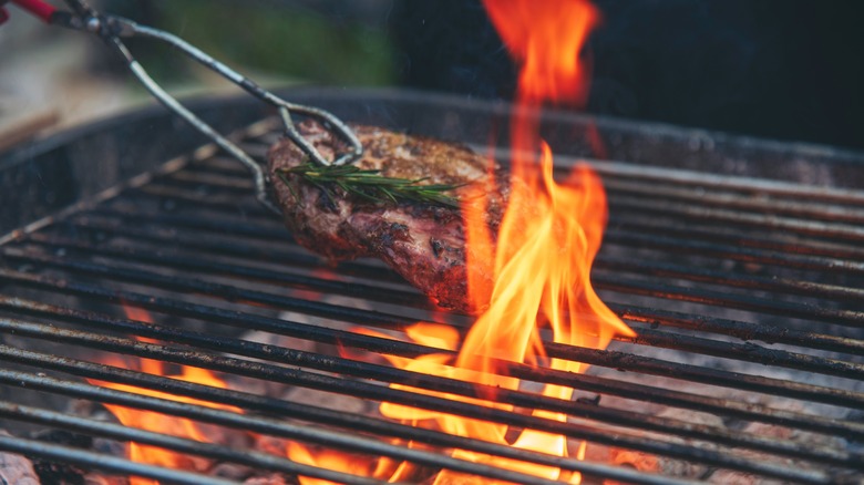 Person grilling meat on hot grill with tongs