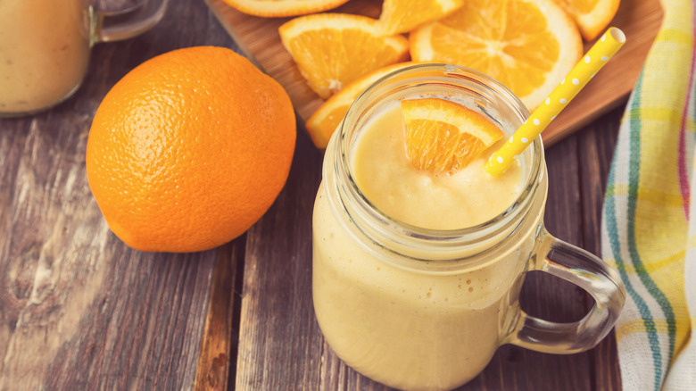 Orange smoothie in a glass mug surrounded by sliced and whole oranges