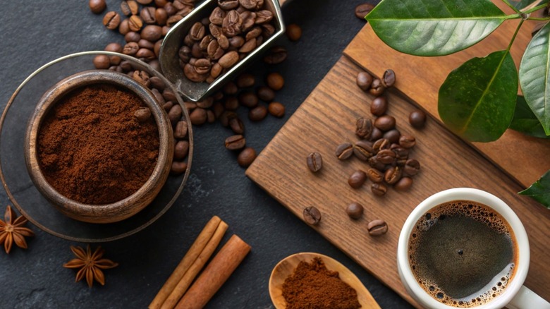 Ground coffee, coffee beans and a cup of coffee laid out together near a cutting board.