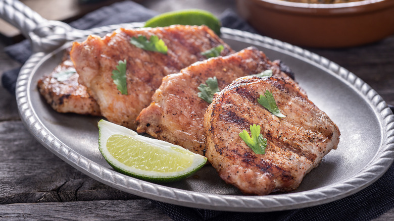 grilled pork hops on a platter garnished with limes