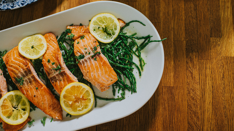 Cooked salmon portions on a plate with lemons and green beans