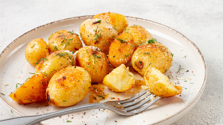 A plate of roasted potatoes on a white plate with a fork