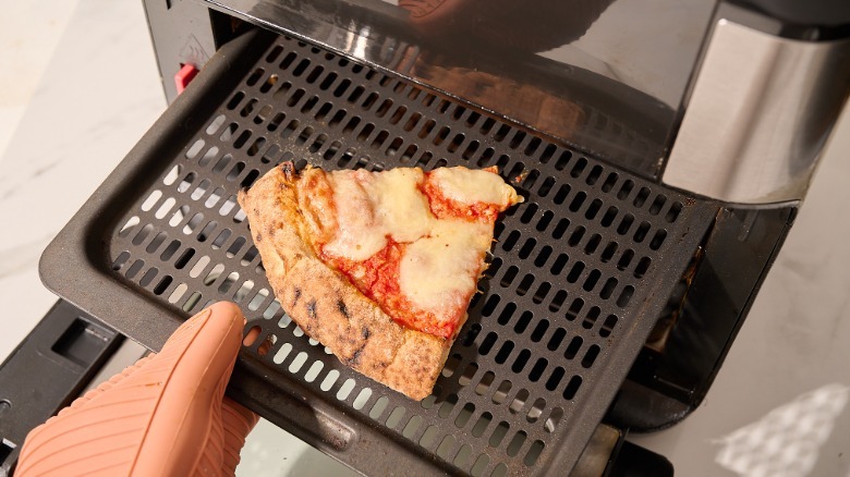 Taking cooked slice of pizza out of air fryer